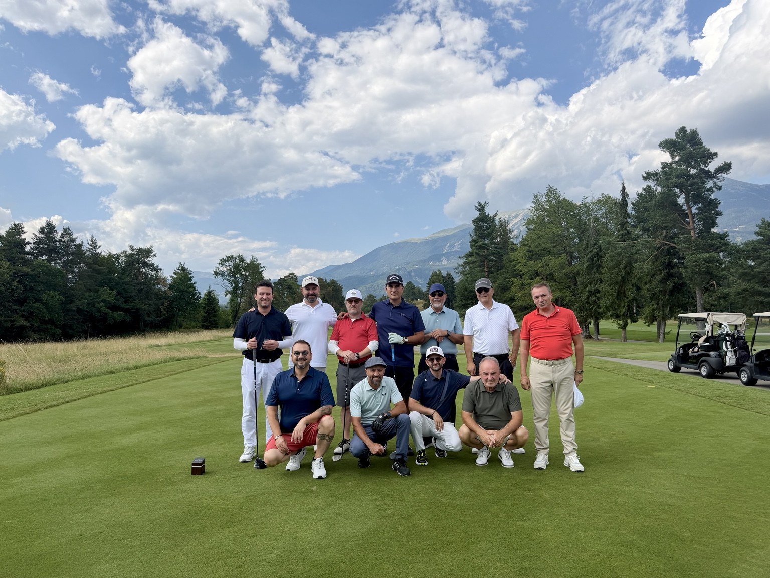 A group of golfers on a tee with mountains in the distance